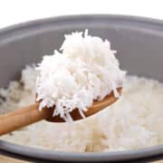 A wooden spoon lifts a serving of fluffy white rice from a pot filled with cooked rice.