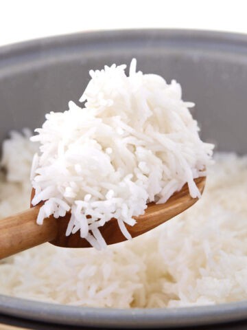 A wooden spoon lifts a serving of fluffy white rice from a pot filled with cooked rice.