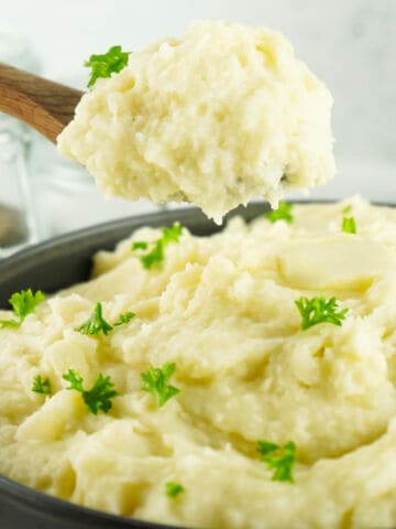 A bowl of creamy copycat Bob Evans mashed potatoes garnished with fresh parsley with a spoon scooping some out.