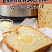 A thick slice of homemade white bread with melted butter sits on a plate, next to a full loaf and a small bowl of butter, in front of a bread machine. Text reads "Basic Bread Machine White Bread.