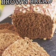 A loaf of brown bread with oats on top is partially sliced on a dark cutting board. Text over the image reads: “Bread Machine Cheesecake Factory Brown Bread.”.