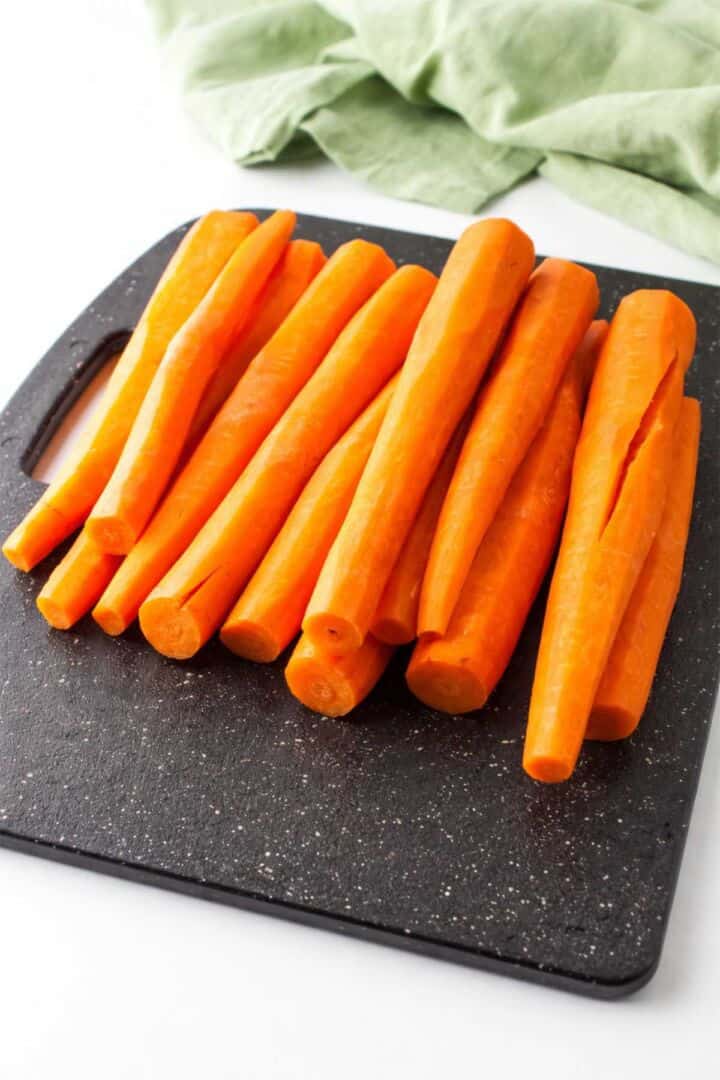 Whole peeled carrots on a black cutting board for Chick-fil-A carrot raisin salad.