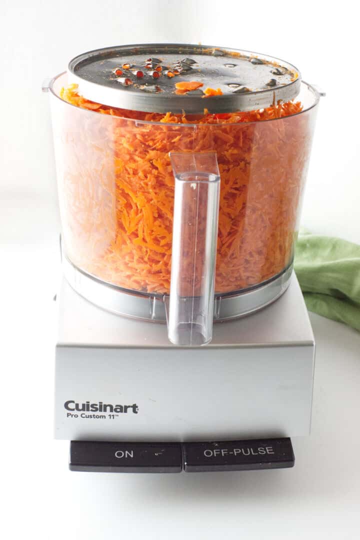 Finely grated carrots in a food processor bowl for carrot raisin salad.