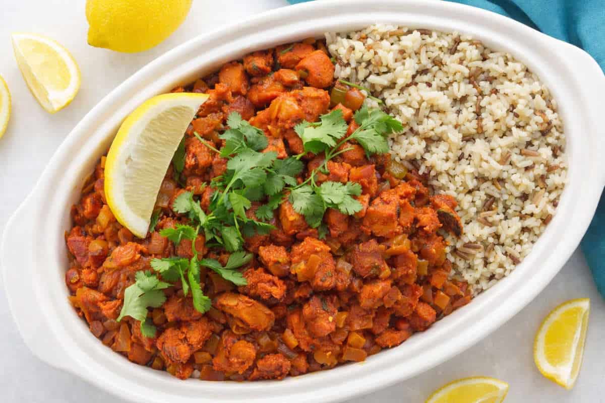 Chicken Mozambique served with rice, cilantro, and a lemon wedge.