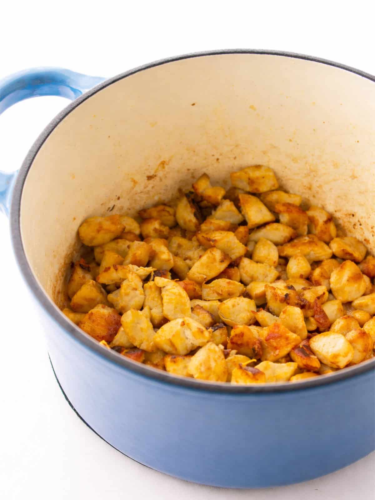 Cubed chicken lightly browning in a blue Dutch oven..