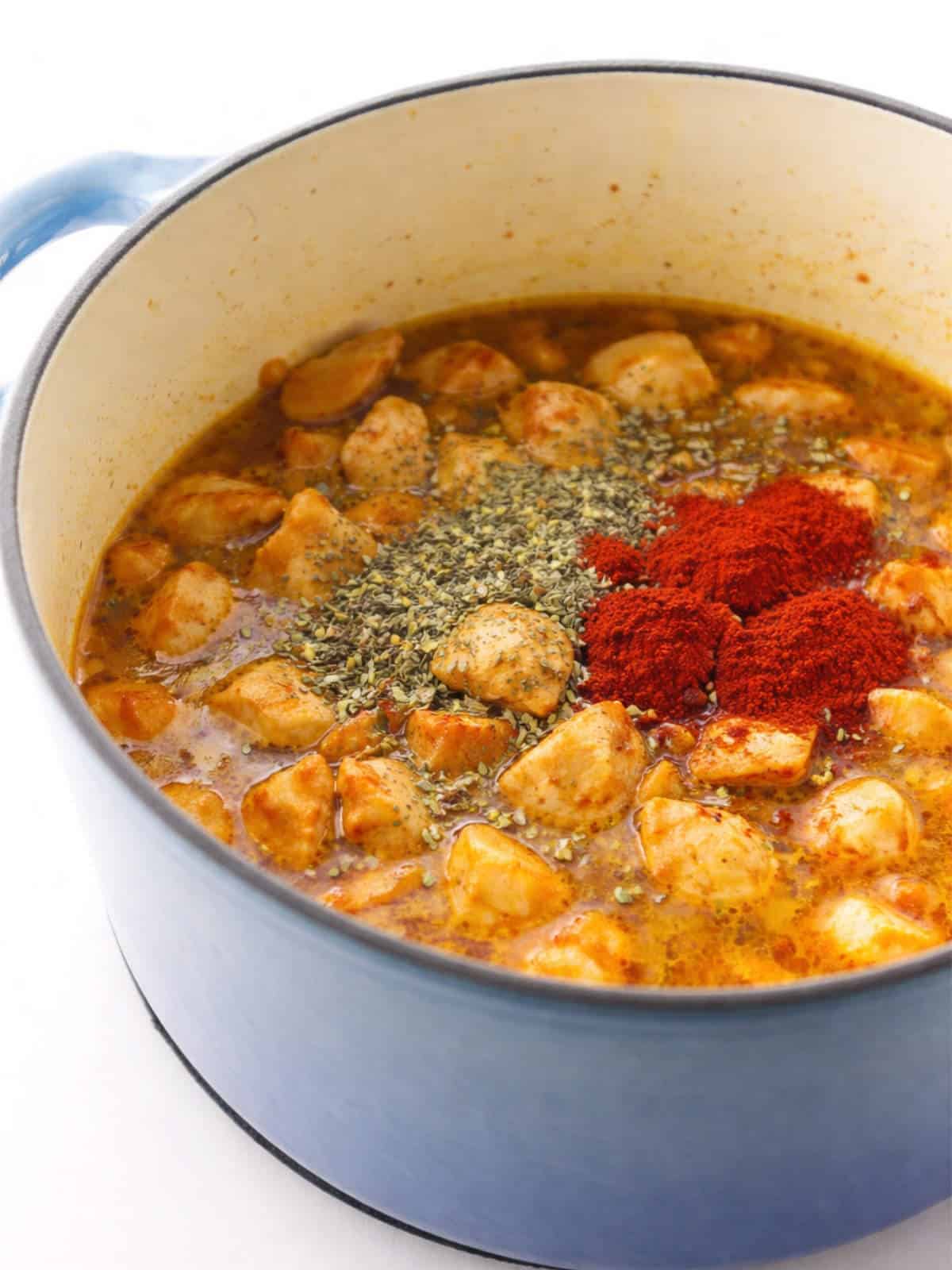 Chicken, broth, and seasonings added to a blue Dutch oven before simmering..