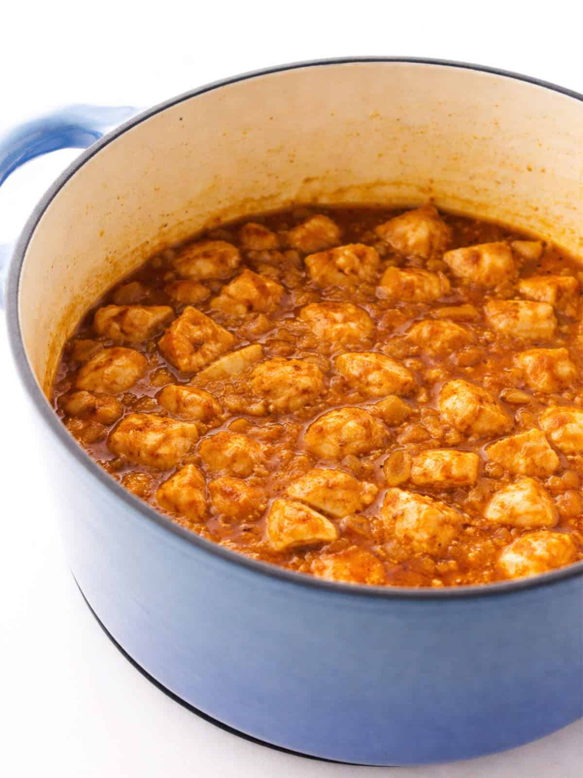 Chicken Mozambique simmering in a blue Dutch oven with a rich sauce..