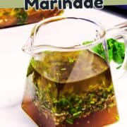 A glass pitcher filled with a green herb and oil marinade sits on a white surface, with text above reading "Easy Lamb Marinade." Fresh herbs are visible inside and next to the pitcher.