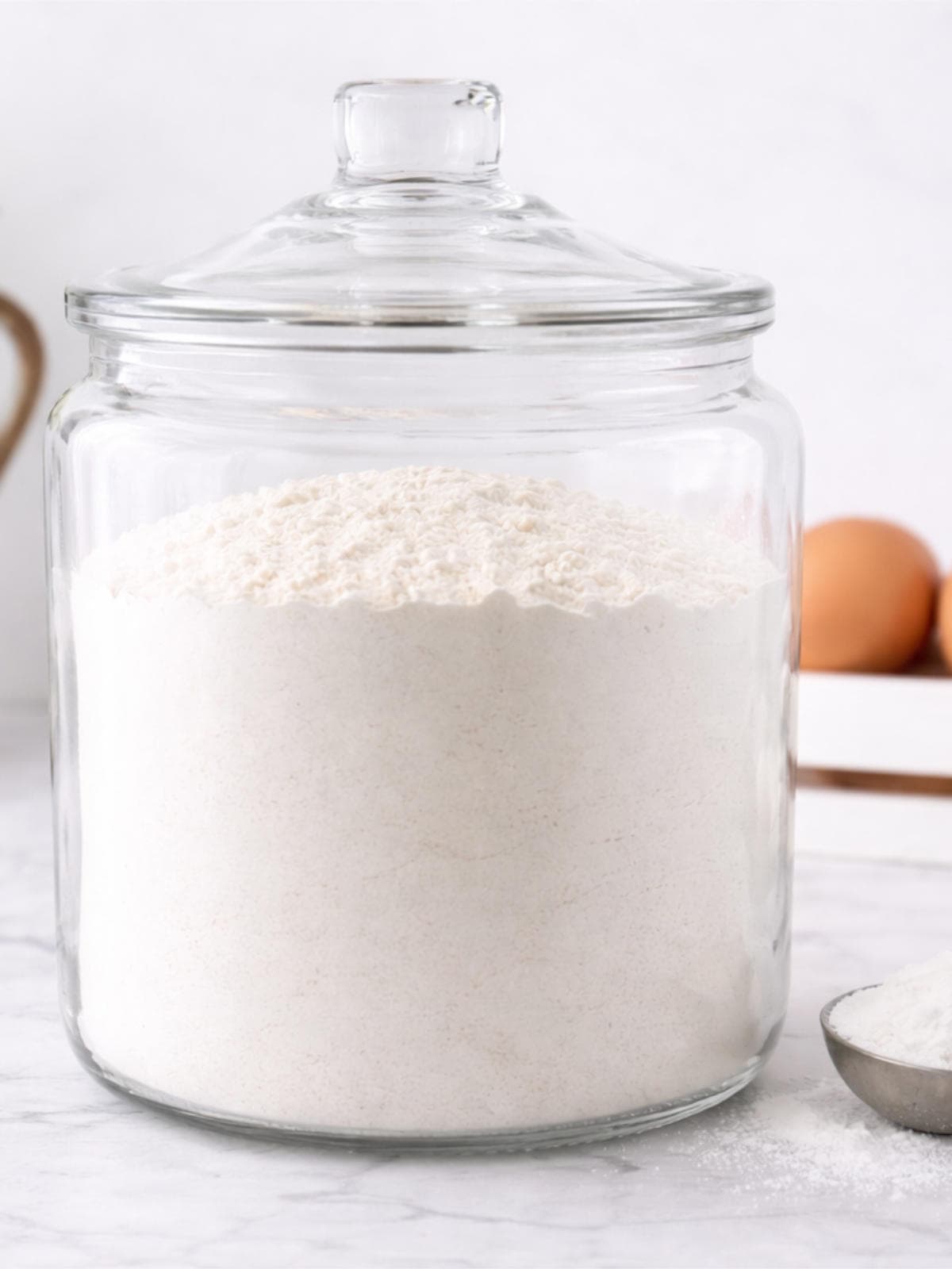 Homemade self rising flour stored in a clear glass jar on a kitchen counter.