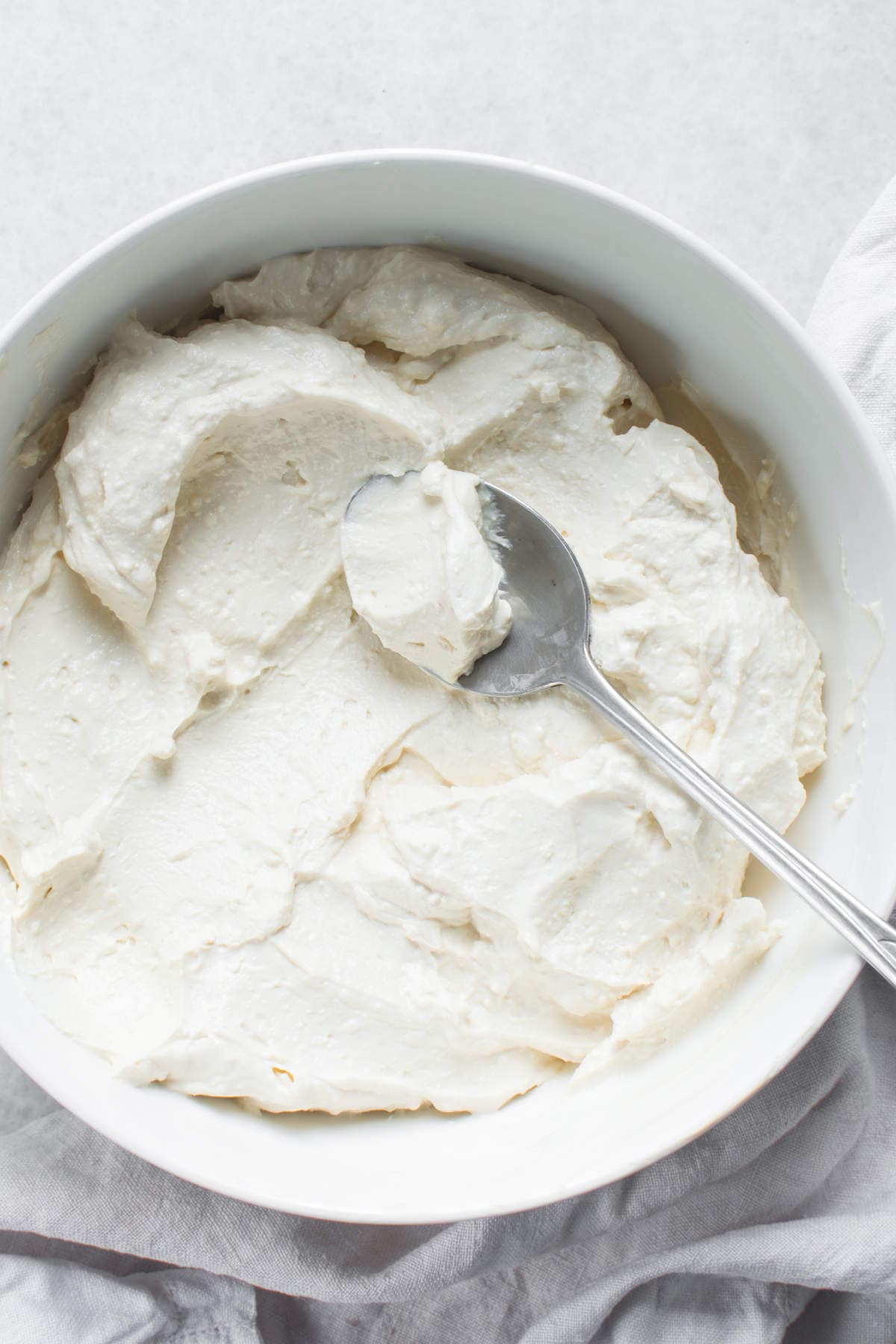 A bowl filled with freshly made homemade Greek yogurt, with a spoon lifting thick spoonful.