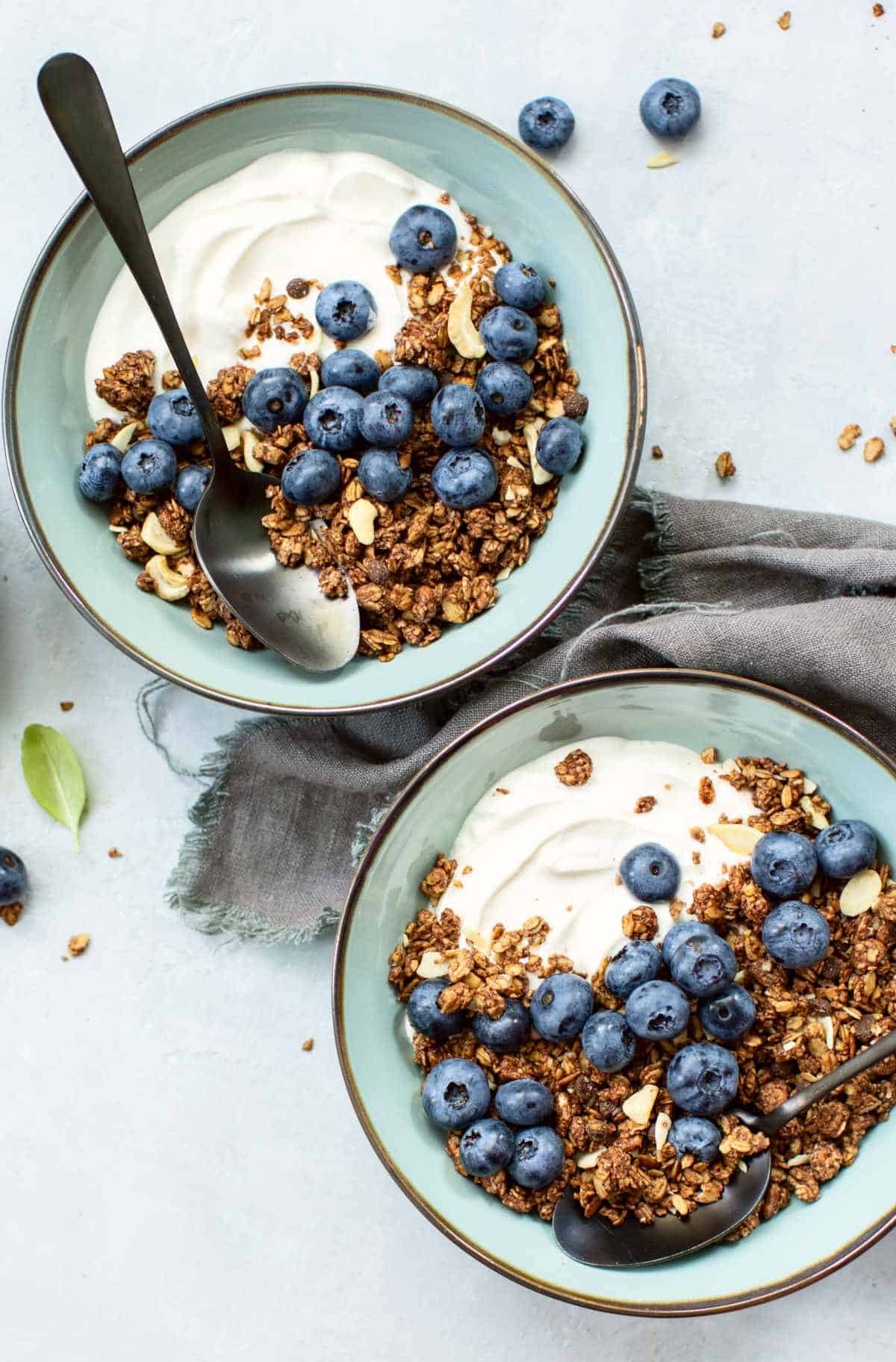 Drizzled honey from a spoon onto a glass of yogurt parfait layered with granola, banana slices, and nuts.
