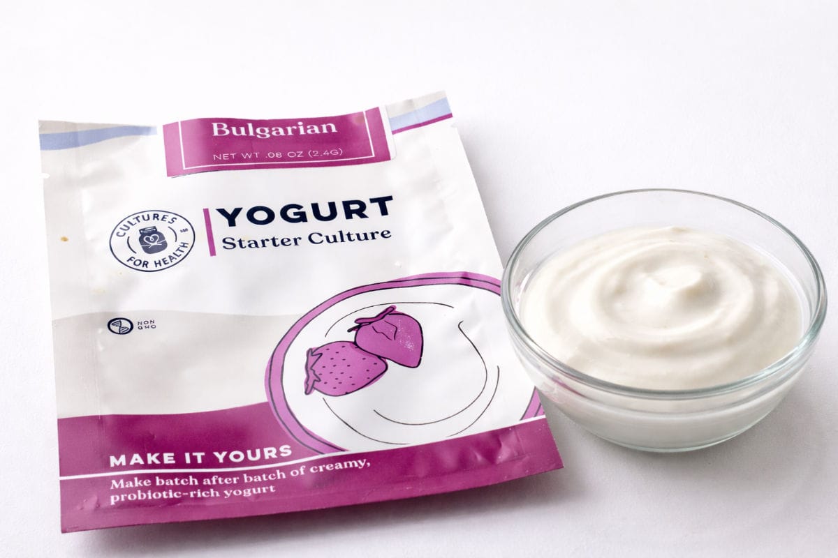 A packet of dry yogurt starter culture and a small glass bowl filled with plain yogurt.