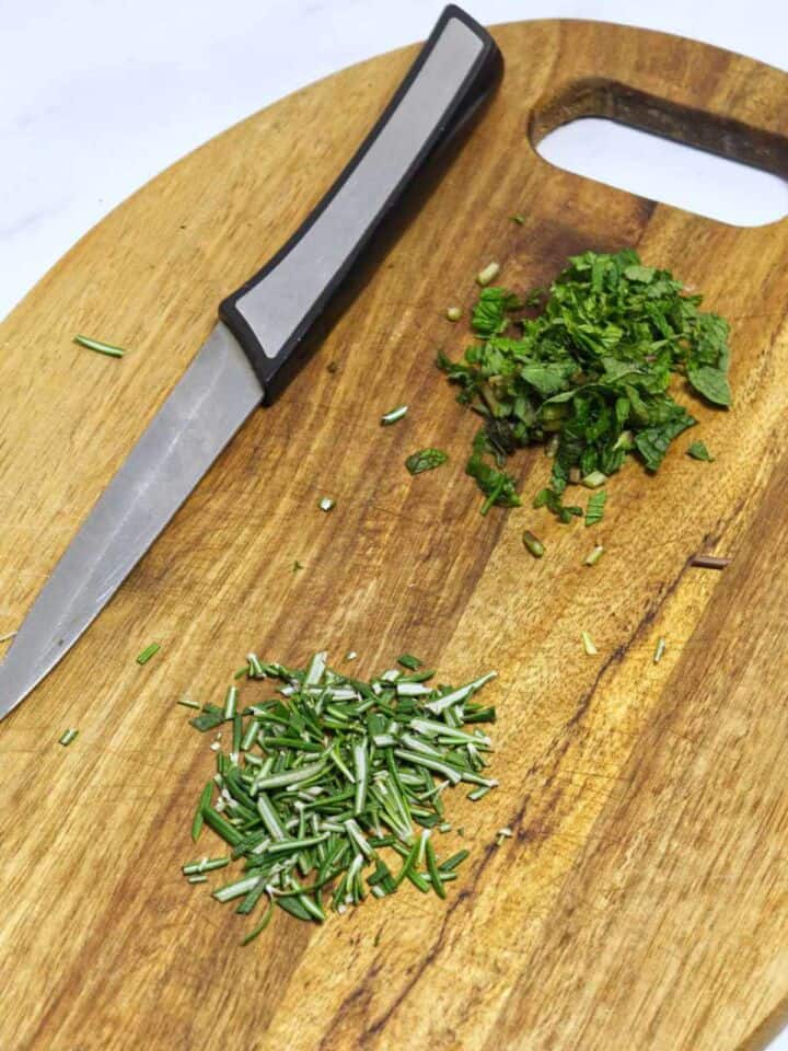 Chopped mint and rosemary for lamb marinade on cutting board.
