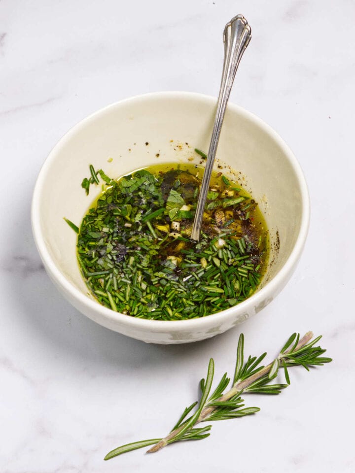 Mixing lamb marinade with herbs, garlic, and olive oil in bowl.