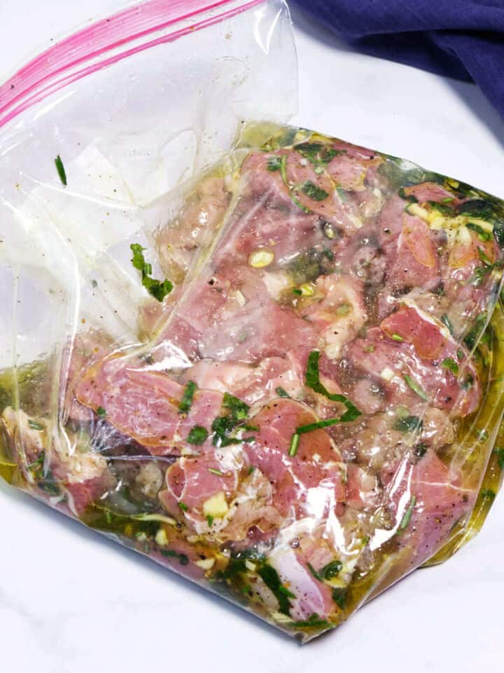 Lamb marinating in herb marinade inside sealed bag.