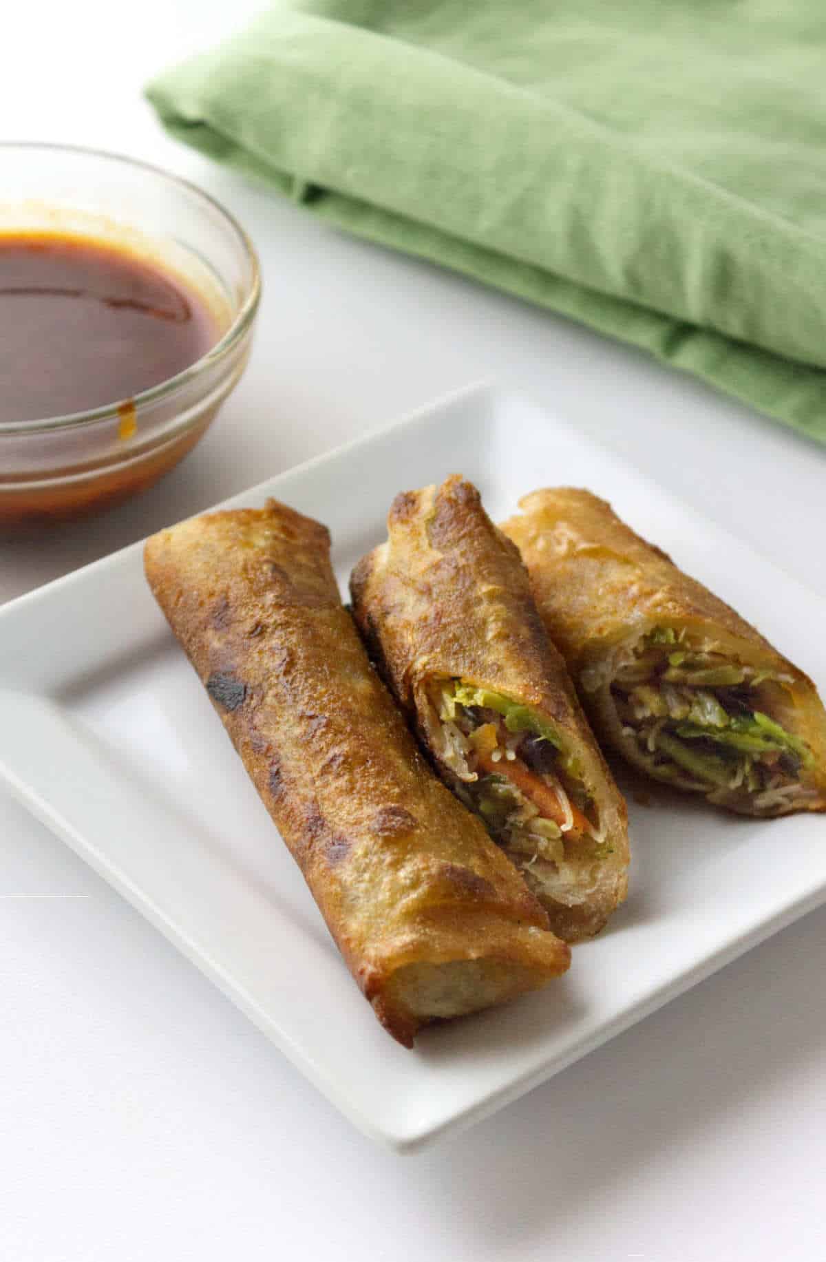 Fresh vegetable lumpia cut open on a white plate with dipping sauce.