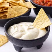Mexican white sauce dip close up with tortilla chip in black bowl.