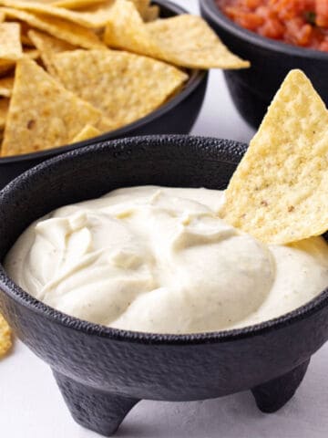 Mexican white sauce dip close up with tortilla chip in black bowl.