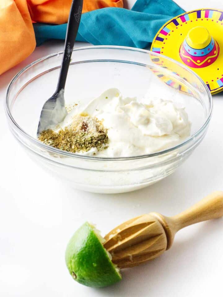 Mixing Mexican white sauce with sour cream and spices in glass bowl.