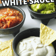 Three black bowls with dips—salsa, guacamole, and creamy white sauce—are surrounded by tortilla chips. Bold text reads "Mexican White Sauce" and the website "smellslikedelish.com" appears at the bottom.