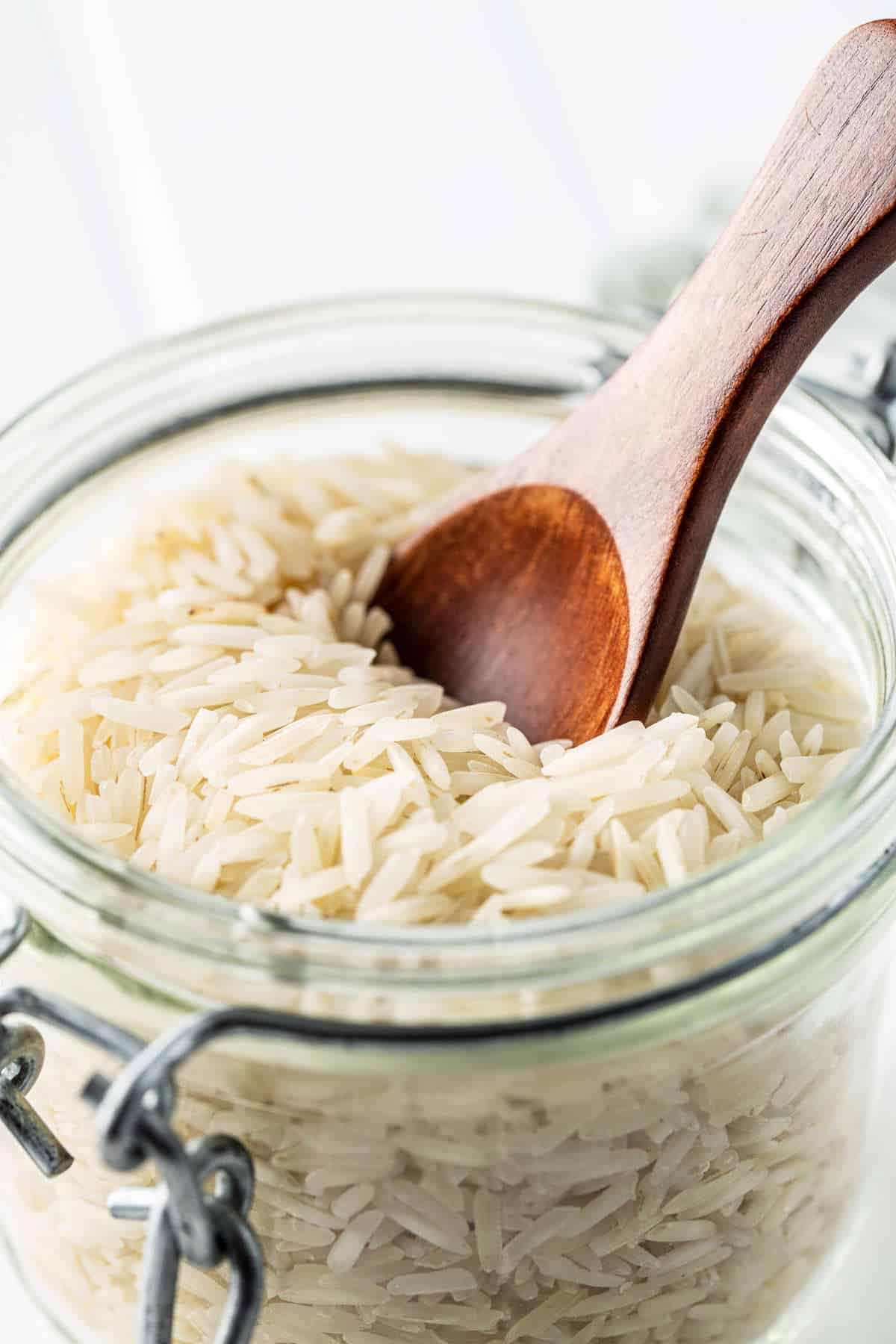 Uncooked basmati rice in a glass jar with a wooden spoon.