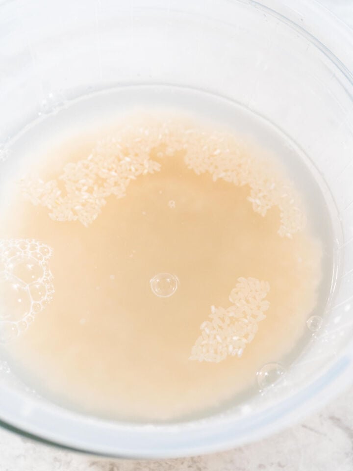 Uncooked basmati rice being rinsed in a strainer under cold water.