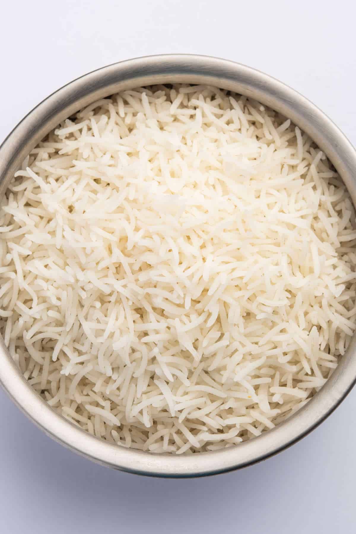 Cooked basmati rice in a rice cooker, showing long fluffy grains in a bowl.