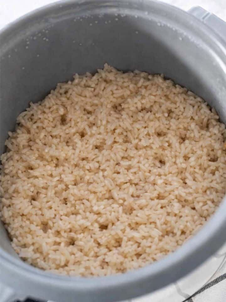 Cooked brown rice in a grey rice cooker, with the rice appearing fluffy and evenly cooked.