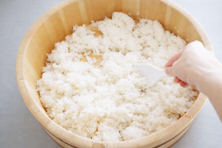 Sushi rice being turned and cooled in wooden hangiri.