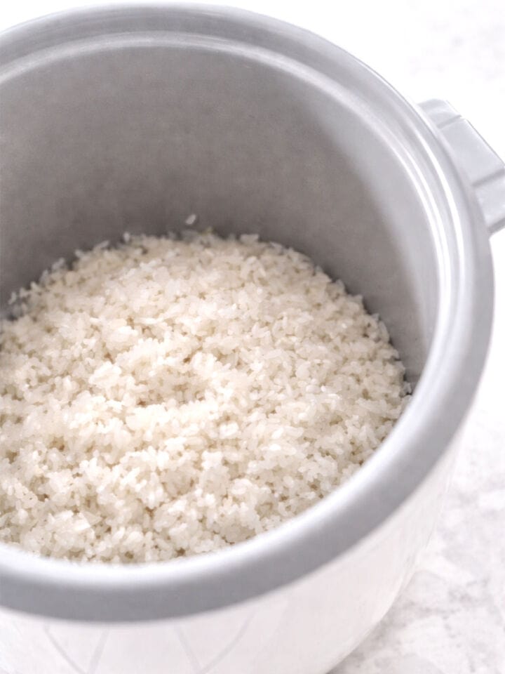 Rinsed sushi rice in rice cooker insert with chalky appearance.