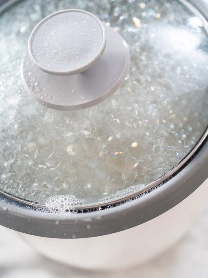 Rice cooker with sushi rice cooking under glass lid.