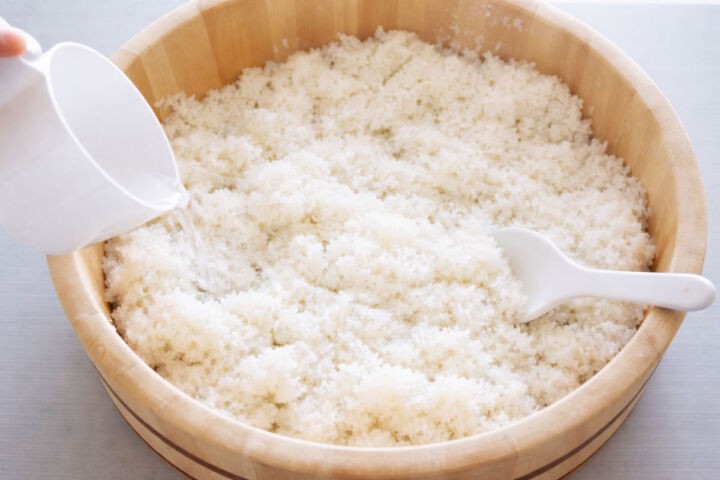 Pouring sushi seasoning onto hot rice cooling in a hangiri.