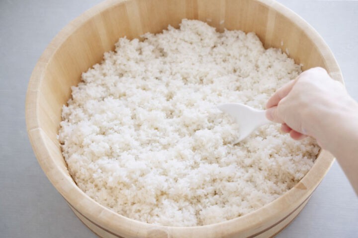 Cooling sushi rice with a rice paddle in a wooden hangiri.