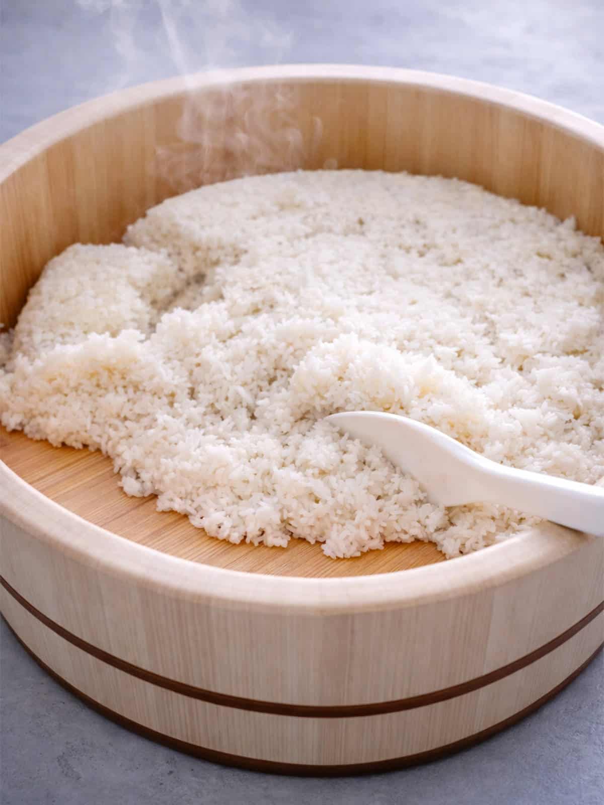 Sushi rice in wooden hangiri with paddle resting on rim.