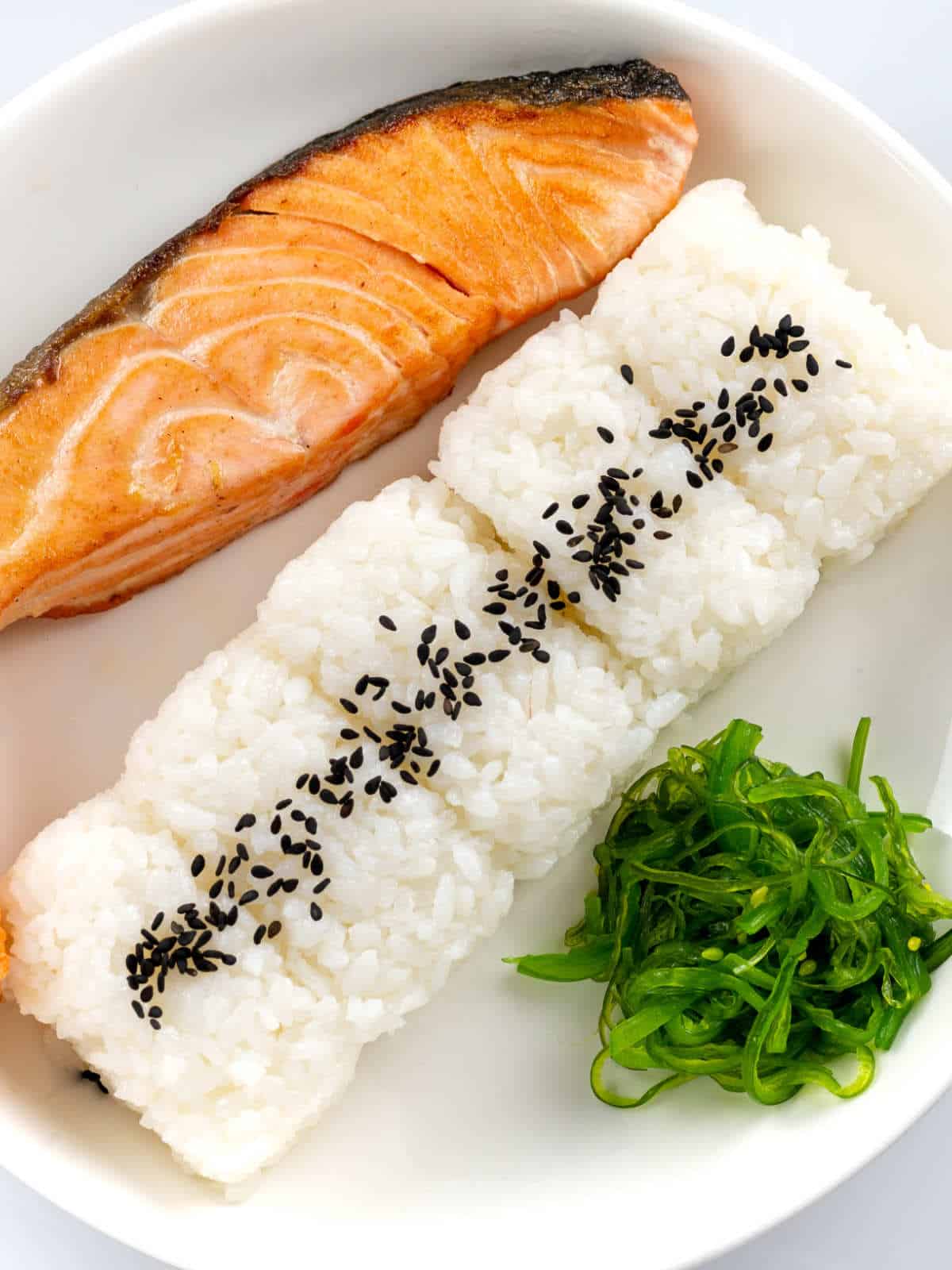 Cooked sushi rice served with grilled salmon and seaweed salad.