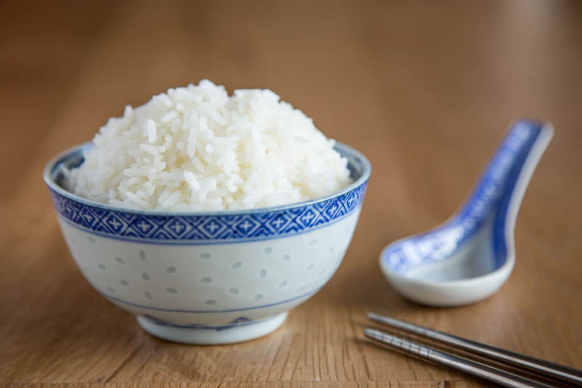 Fluffy jasmine rice in bowl with chopsticks on wooden table.