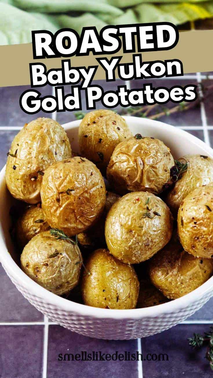 A white bowl filled with roasted baby Yukon Gold potatoes sits on a tiled surface. The potatoes have crispy, golden skin and are garnished with herbs. Text above the bowl reads, "ROASTED Baby Yukon Gold Potatoes.