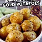 A white bowl filled with roasted baby Yukon gold potatoes sits on a tiled surface, with a seasoning container blurred in the background. Bold text over the image reads "Roasted Baby Yukon Gold Potatoes.