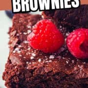 Close-up of a sheet pan brownie topped with flaky sea salt and fresh raspberries on a white plate. Text at the top reads "Sheet Pan Brownies" and "smellslikedelish.com" is at the bottom.