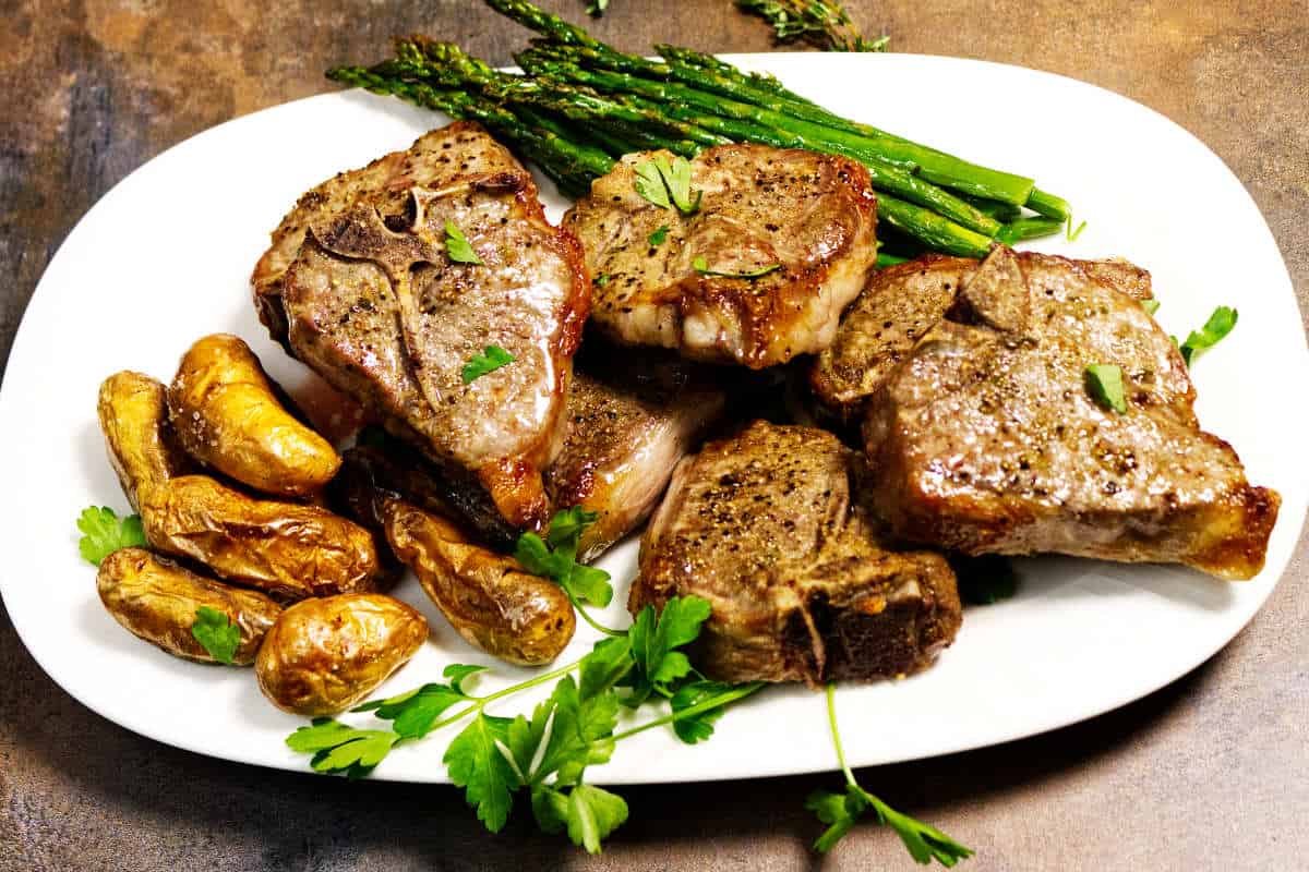Platter of air fryer lamb chops served with roasted potatoes, asparagus, and fresh herbs.