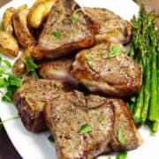Air fryer lamb chops served with roasted potatoes and asparagus on a white plate.
