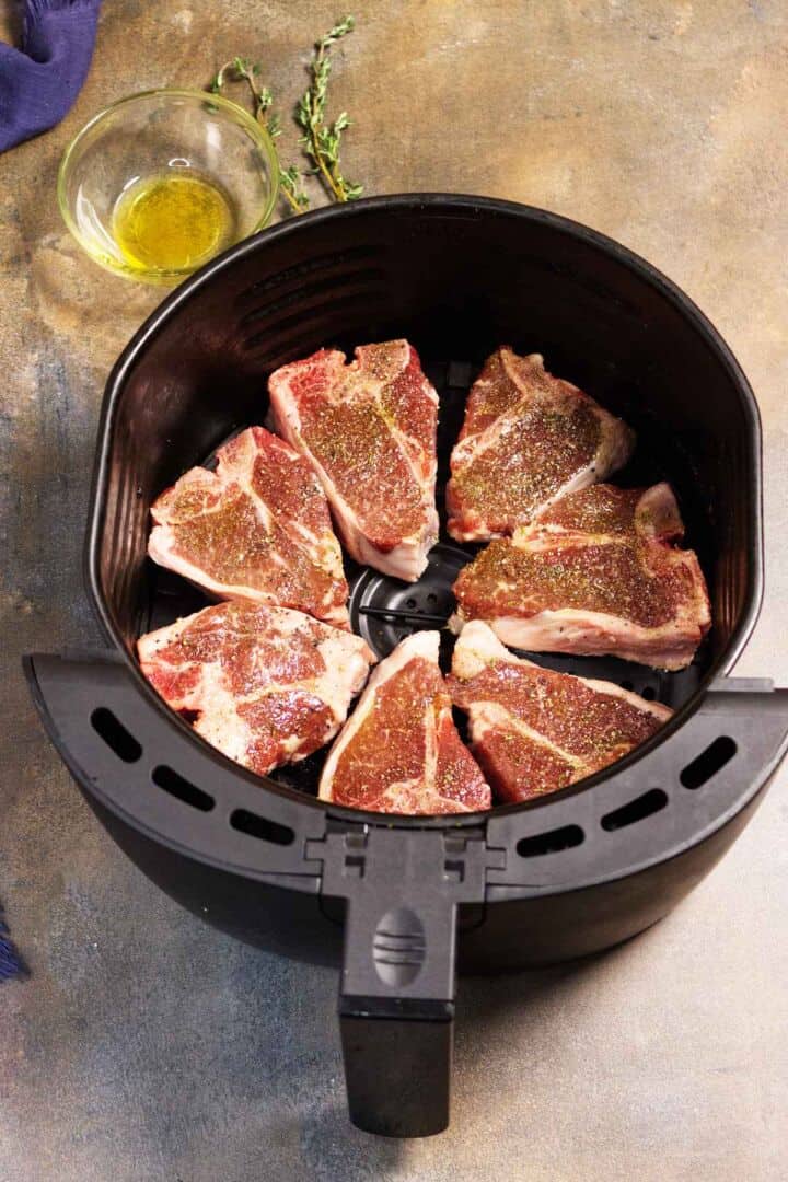 Seasoned lamb loin chops arranged in a single layer inside an open air fryer basket.