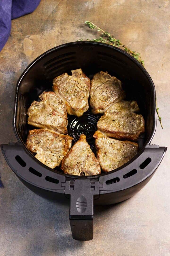 Lamb loin chops cooking in the air fryer basket with browned edges starting to form.
