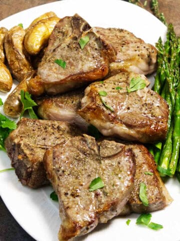 Grilled lamb chops, fingerling potatoes, and asparagus on a white plate, topped with fresh parsley.