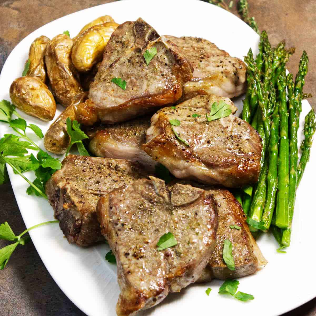 Cooked air fryer lamb chops with browned edges, potatoes, and asparagus on a serving plate.