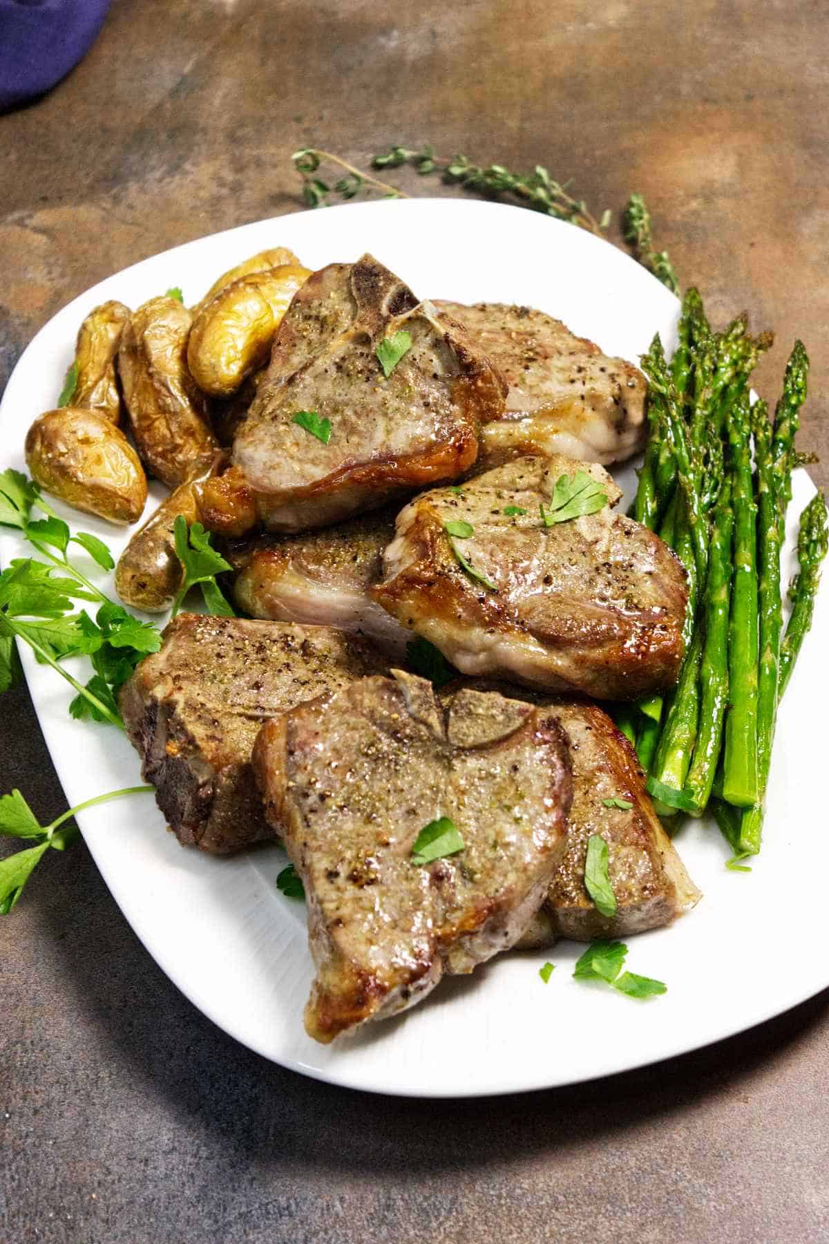 Air fryer lamb chops served with roasted potatoes and asparagus on a white plate.