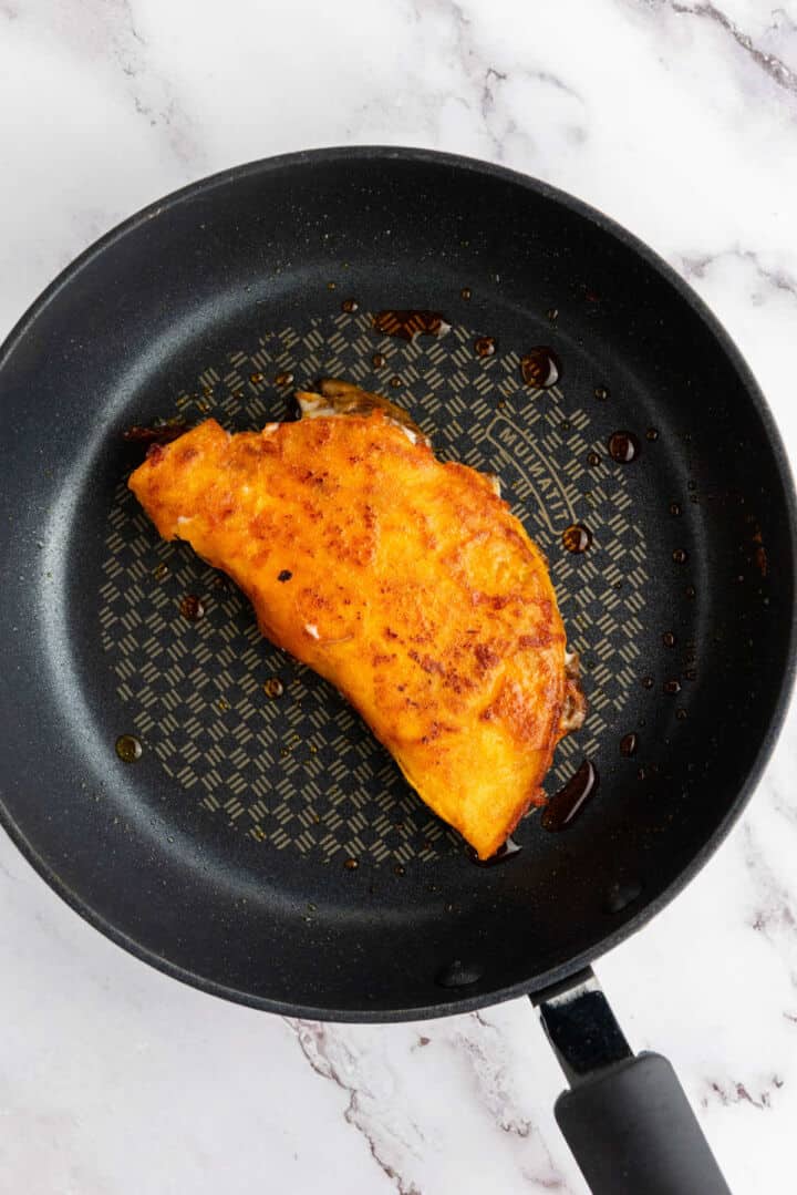 A golden-brown folded birria quesadilla is cooking in a nonstick skillet.
