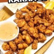 A platter of golden, crispy chicken karaage pieces served with dipping sauce, lemon wedges, and a side of shredded cabbage on a white plate. The text "CHICKEN KARAAGE" is at the top.