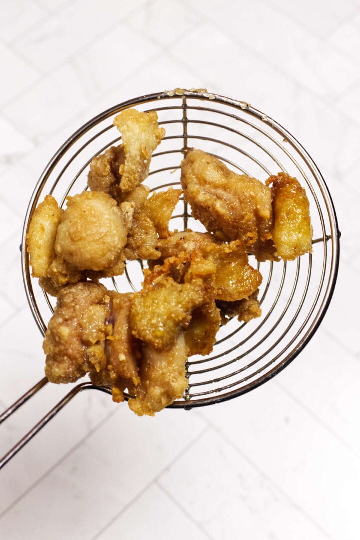 Freshly fried chicken karaage lifted from the oil with a wire skimmer.