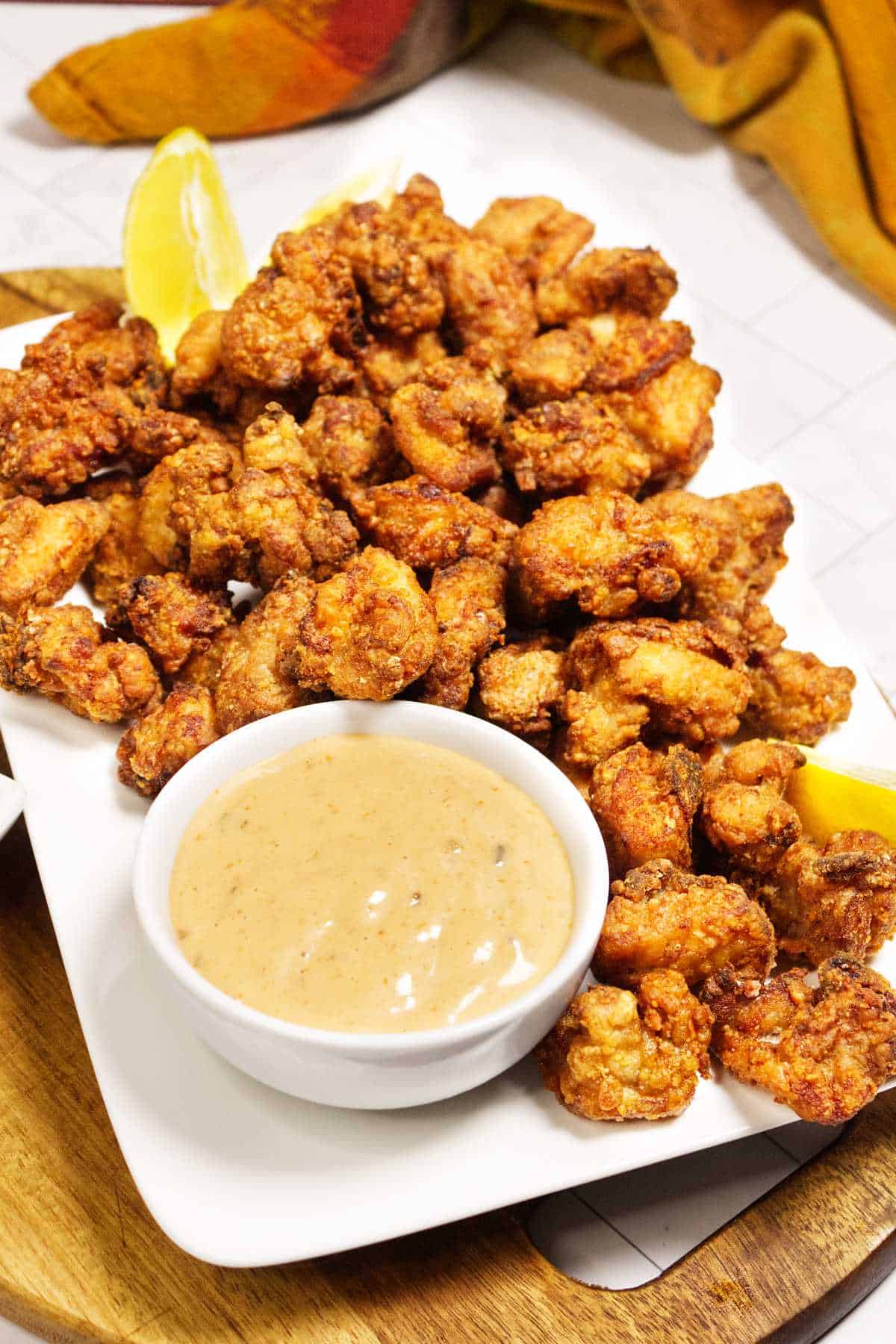 A white plate of crispy chicken karaage served with a creamy dipping sauce and lemon wedges.